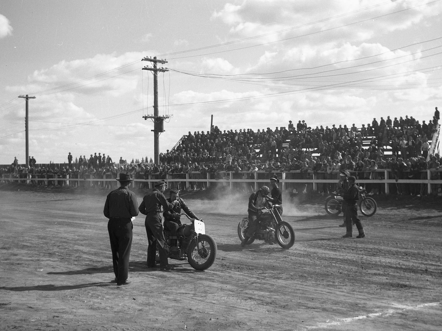 Ace-Hy racers on motorcycles at a dirt track in front of a packed grandstand